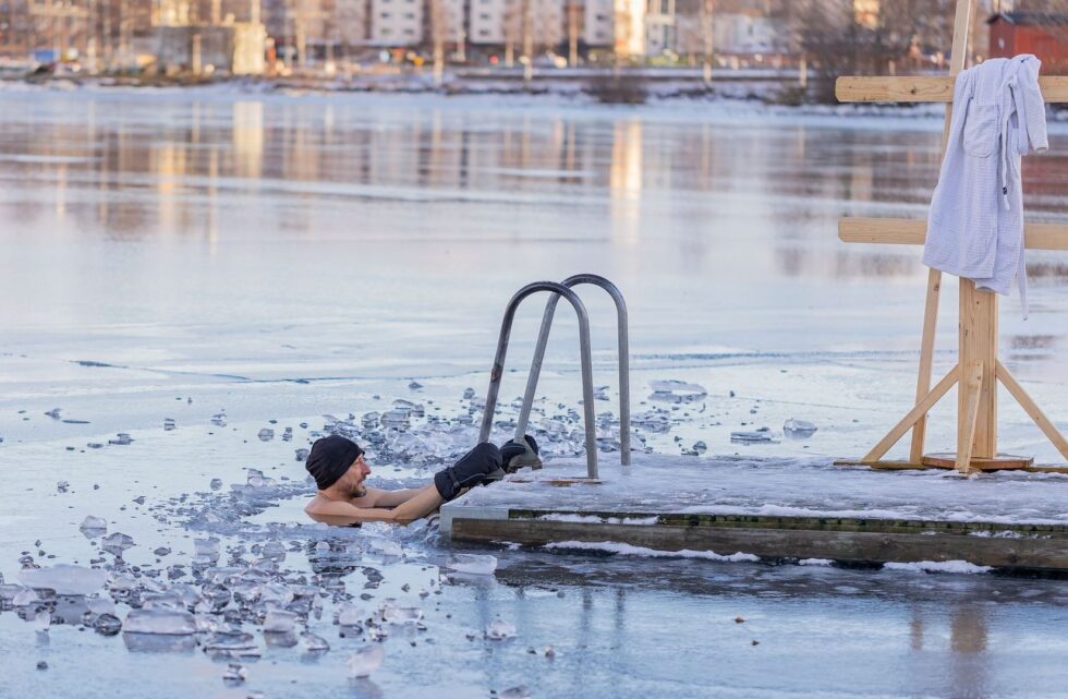 Person tar ett kallt isbad vid en stege i fruset vatten